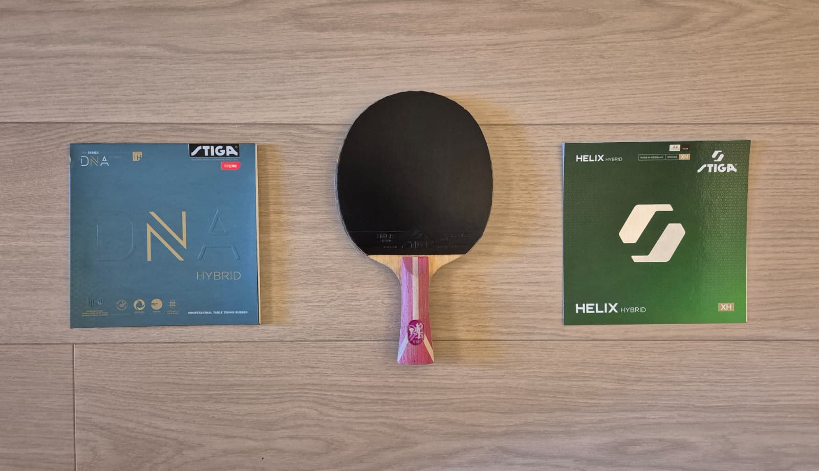 Stiga DNA Hybrid H and Helix Hybrid XH packages beside a table tennis racket on a wooden table